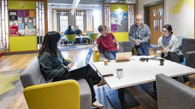 A group of postgraduate students working and chatting together in a modern campus social space.