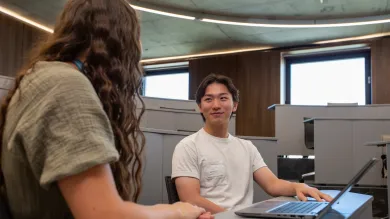 Student speaking with a careers adviser while using a laptop in a campus study space.
