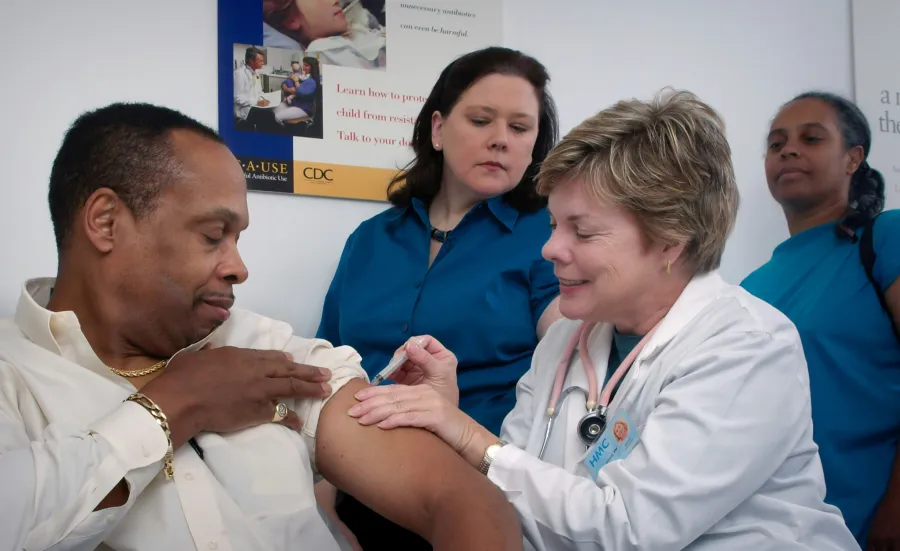 A doctor gives a man a vaccination while onlookers watch