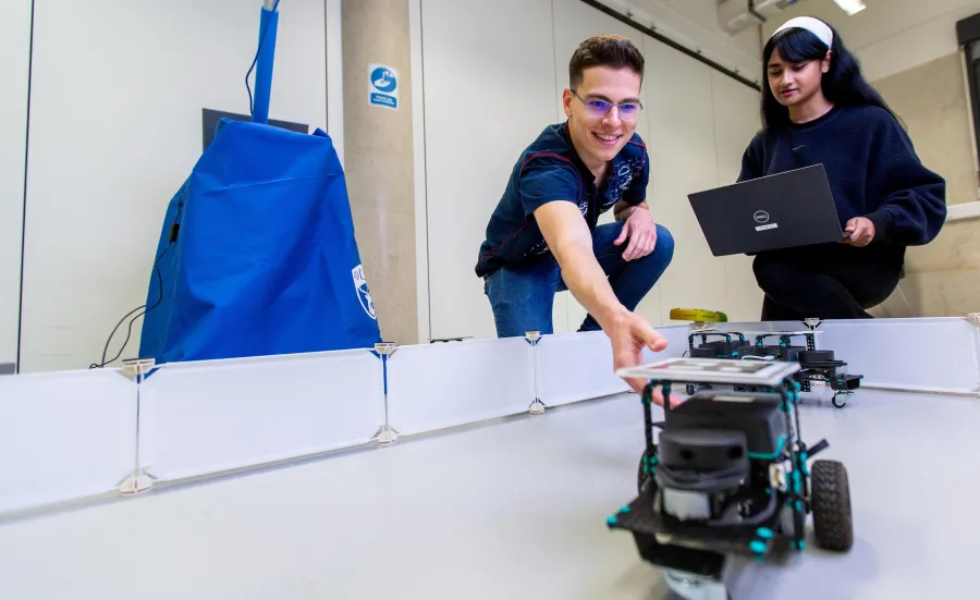 Two students testing a small mobile robot within a bounded arena in university robotics lab.