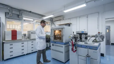 Scientist in a lab coat handling a metal tray and operating laboratory equipment in a bright research laboratory.