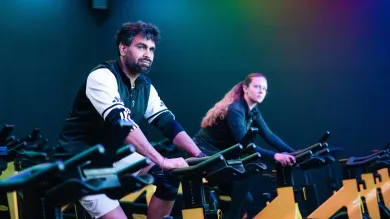 Two people taking part in an indoor spin cycling class on stationary bikes.