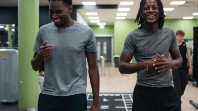 Two students walking through a university gym after exercising, smiling and wearing sportswear.