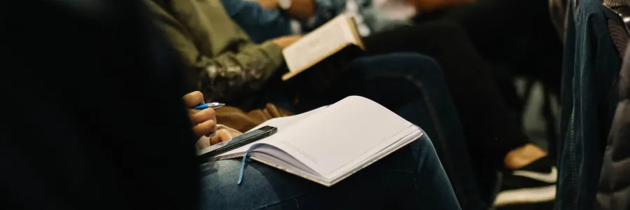 Looking along a row of people at a seminar. We can't see their faces. Some of them are taking notes.