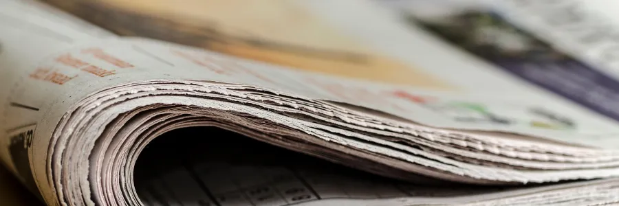 A rolled-up newspaper on a wooden surface, with visible pages and text.