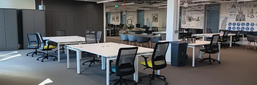 Modern open office space with white desks, black chairs, grey cabinets, and a collaborative area with murals.