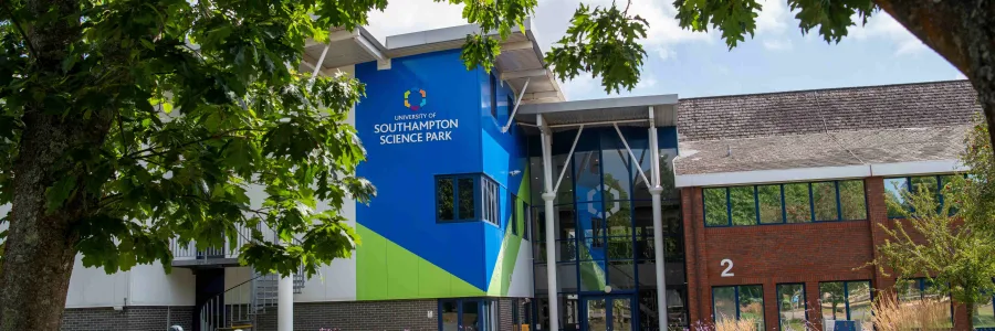 An exterior view of the main building at the Science Park. It is a sunny day and there are 2 cyclists on the road in front of the building.