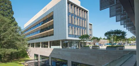 Exterior shot of modern building, surrounded by grass and trees, on a sunny day.