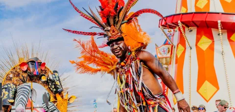 A smiling, vibrantly-dressed performer on stilts.