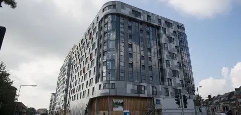 Tall, metal and glass apartment building surrounded by shops and roads.