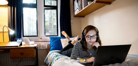 Student laying on bed, working on laptop.
