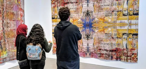 Three students admire a large piece of contemporary artwork hung on a gallery wall.