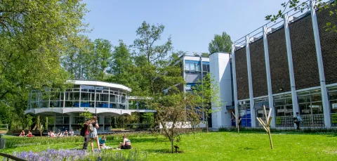 Modern looking campus building with, students relaxing on a grassy area in the foreground.