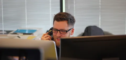 Man on phone in student support, looking over the top of a computer. 
