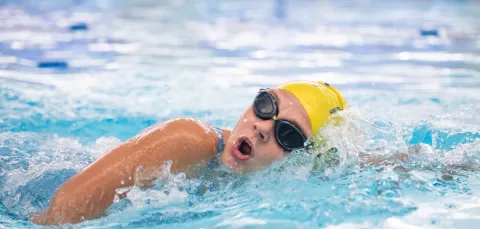 A swimmer in goggles and yellow cap cuts through the water while swimming in a pool.