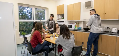 A group of students talking and cooking in a halls kitchen.