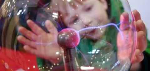 Young child with hands placed on glass electricity ball