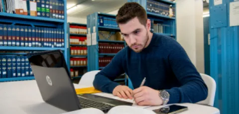A male student studying at his laptop in the library.