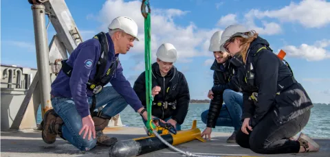 Several students at sea, crouching around an autonomous marine drone.