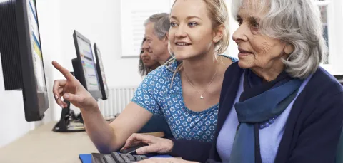 Several students sitting in pairs with elderly people, working together at computers.