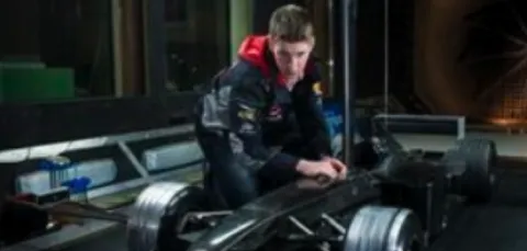 A male student kneeling beside a half-scale model of a Formula 1 car, adjusting various controls.