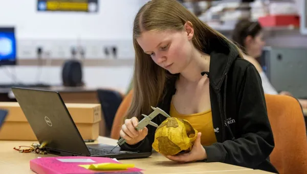 An archaeology student examines an object at a table, using a measuring device