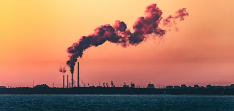 A shot of an industrial shoreline silhouetted at sunset, with smoke from a refinery curling into the sky.