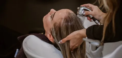 A hairdresser washes a client's hair at a basin