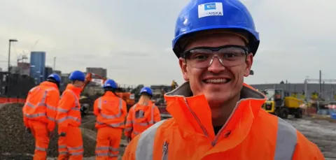 A group of engineering students in overalls and hard hats in an industrial setting