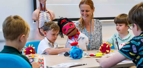 A group of primary school students doing educational activities around a table, with supervision from a member of staff.