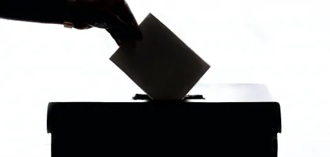 A silhouette of somebody's hand placing their vote into the polling booth box