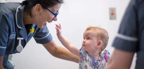 Baby reaches up towards smiling research nurse 