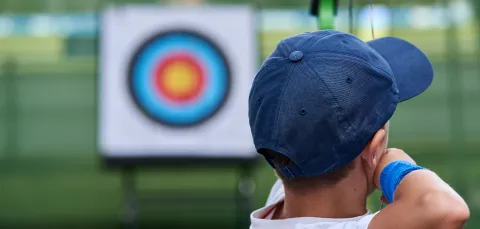 Close up of a child, seen from behind, about to shoot an arrow at an archery target.