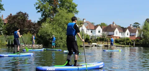 A group of young people paddleboarding on a river on a sunny day
