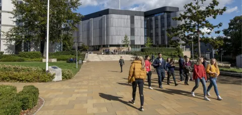 Students walk on a sunny campus with modern buildings and greenery