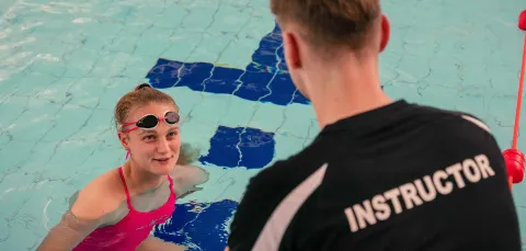 An instructor on the pool side talking to a swimmer in the pool