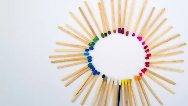 Circle of multicolored matchstick tips arranged in a rainbow gradient on a white background, creating a radial pattern.