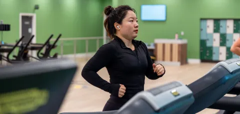 A woman with her hair tied up and earpods running on a treadmil in the gym.