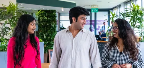 Three students are talking with each other while walking down a bright university campus corridor.