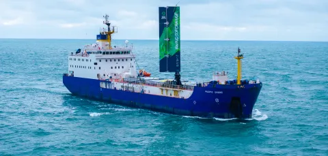 A large cargo vessel sailing on the ocean. It has a 20 metre-high wing sail. 