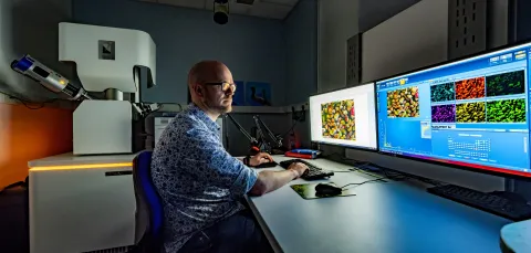 A scientist sits at a bank of computer screens performing scanning electron microscopy