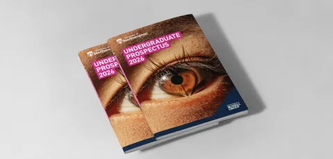A small stack of university prospectuses on a table. The front cover of the prospectus reads 'Undergraduate Prospectus 2026' and features a close-up image of an eye, with the reflection of an open book.