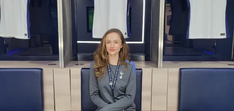 Emma Green wearing a Tottenham Hotspur tracksuit, is sitting on a chair with 3 Tottenham Hotspur shirts hanging behind her.