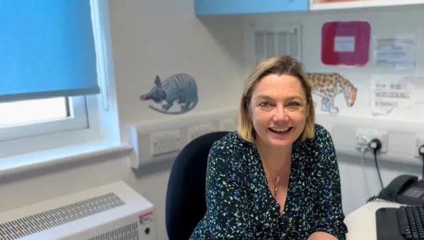 Professor Juliet Gray sitting at her desk, smiling. There are pangolin and leopard stickers on a white wall in the background. The window behind her is mostly covered by a light blue blind.