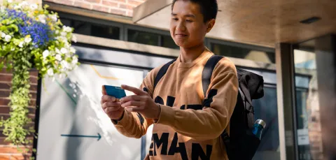 A student holding their ID card while stood outside the entrance to University of Southampton's Student Hub.
