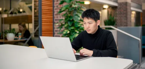 A student sat at a desk in the University of Southampton's Student Hub, with a laptop open on the desk.