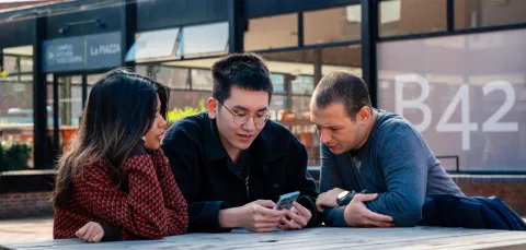 Three students sat on a bench outside the University of Southampton's students' union. They are a looking at a smartphone held by the student in the middle.