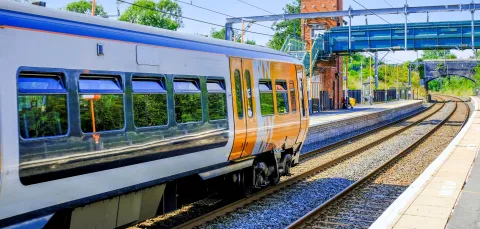 A modern passenger train pulling into a quiet railway station on a sunny day.
