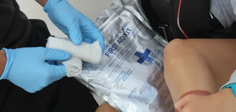 A person wearing blue latex gloves unravelling a bandage from a first aid kit to apply to a leg injury of a passenger onboard a boat.