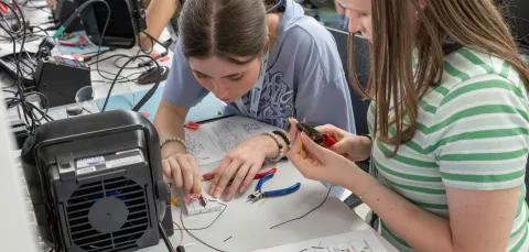 Two young people sitting at a workstation assembling an electronic circuit. 